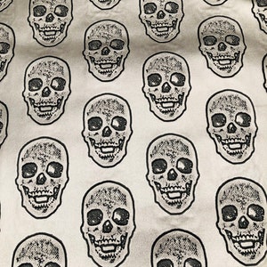 Może przedstawiać: Biała tkanina z powtarzającym się wzorem czarnych czaszek. Czaszki są szczegółowo wykonane z fakturowanym, błyszczącym wykończeniem.
