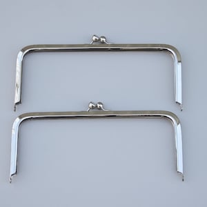 Può includere: Due telai per borse argentati con la parte superiore arrotondata e due piccole sfere decorative. I telai sono progettati per essere utilizzati per creare una borsa o un portafoglio.