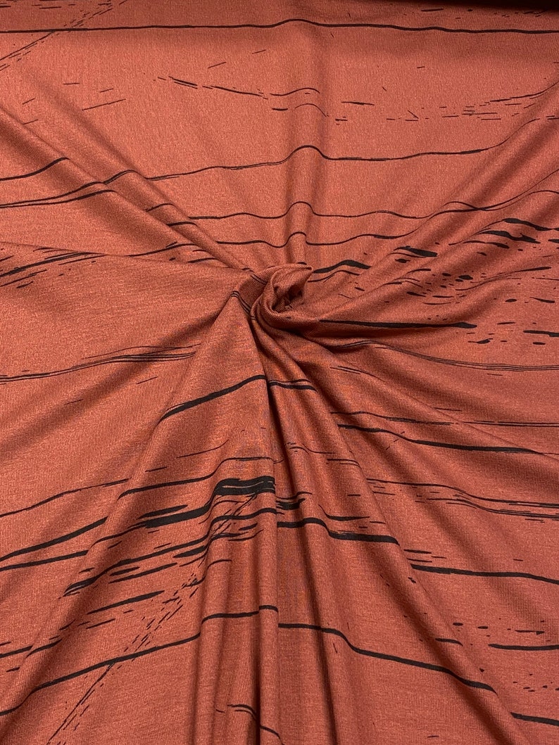 Pode incluir: Tecido vermelho com um padr&atilde;o de gr&atilde;o de madeira preto. O tecido est&aacute; dobrado e torcido, mostrando a textura do material.