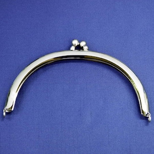 Könnte beinhalten: Silberfarbener Metallrahmen für eine Handtasche mit abgerundetem Oberteil und zwei Haken an jeder Seite. Der Rahmen ist für eine Handtasche oder Clutch konzipiert.