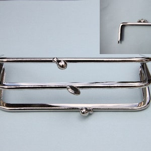 Könnte beinhalten: Drei silberfarbene Handtaschenrahmen, die übereinander gestapelt sind. Die Rahmen sind aus Metall und haben eine abgerundete Form. Jeder Rahmen hat einen kleinen, runden Knopf oben.