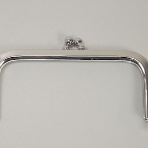 Könnte beinhalten: Silberfarbener Metallrahmen für eine Handtasche mit zwei runden Zierknöpfen oben.