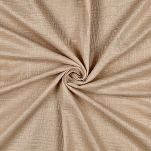 May include: A close-up of a soft, beige fabric with a subtle shimmer. The fabric is wrinkled and folded, creating a textured look.