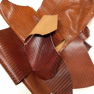 May include: A pile of brown leather pieces with a woven texture. The leather is folded and overlapping.