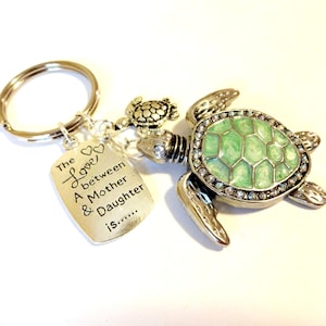 May include: Silver key chain with a green turtle charm and a silver tag that reads "The love between a mother & daughter is..."