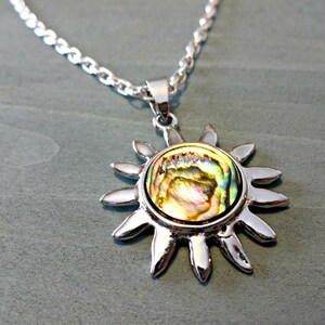 Op de afbeelding: Een zilveren ketting met een zon hanger met een iriserende abalone schelp inlay.
