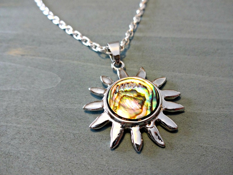 Op de afbeelding: Een zilveren ketting met een zon hanger met een iriserende abalone schelp inlay.