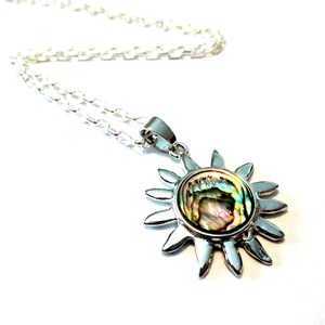 Op de afbeelding: Een zilveren ketting met een zon hanger met een iriserende abalone schelp inlay.