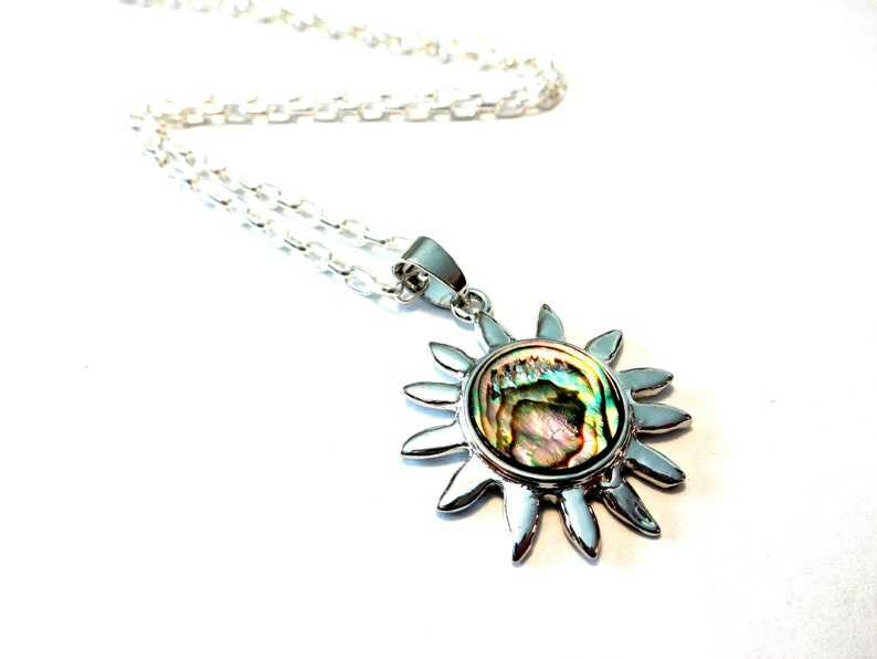 Op de afbeelding: Een zilveren ketting met een zon hanger met een iriserende abalone schelp inlay.