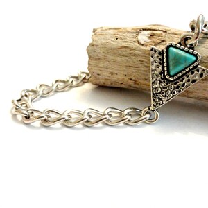May include: A silver chain bracelet with a turquoise triangle pendant. The pendant has a textured silver design.