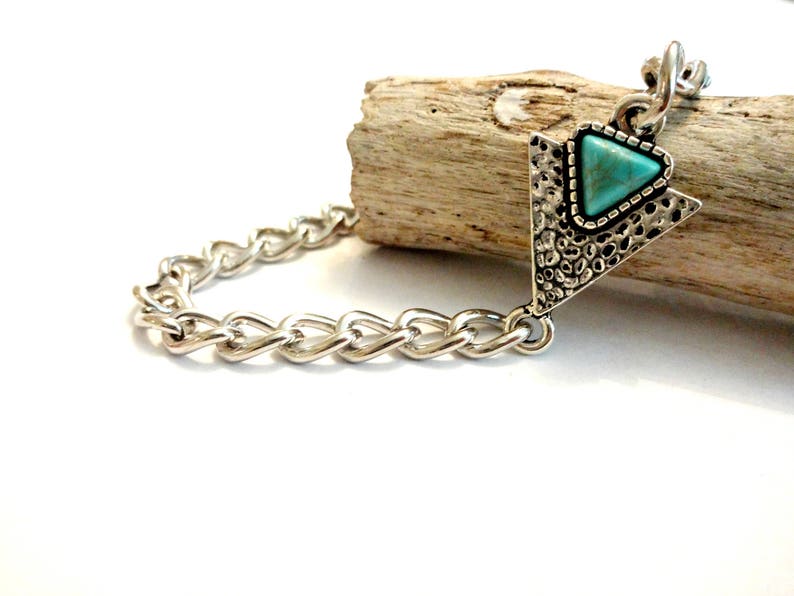 May include: A silver chain bracelet with a turquoise triangle pendant. The pendant has a textured silver design.