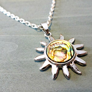 Op de afbeelding: Een zilveren ketting met een zon hanger met een iriserende abalone schelp inlay.