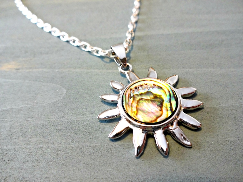 Op de afbeelding: Een zilveren ketting met een zon hanger met een iriserende abalone schelp inlay.