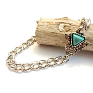 May include: A silver chain bracelet with a turquoise triangle pendant. The pendant has a textured silver design.