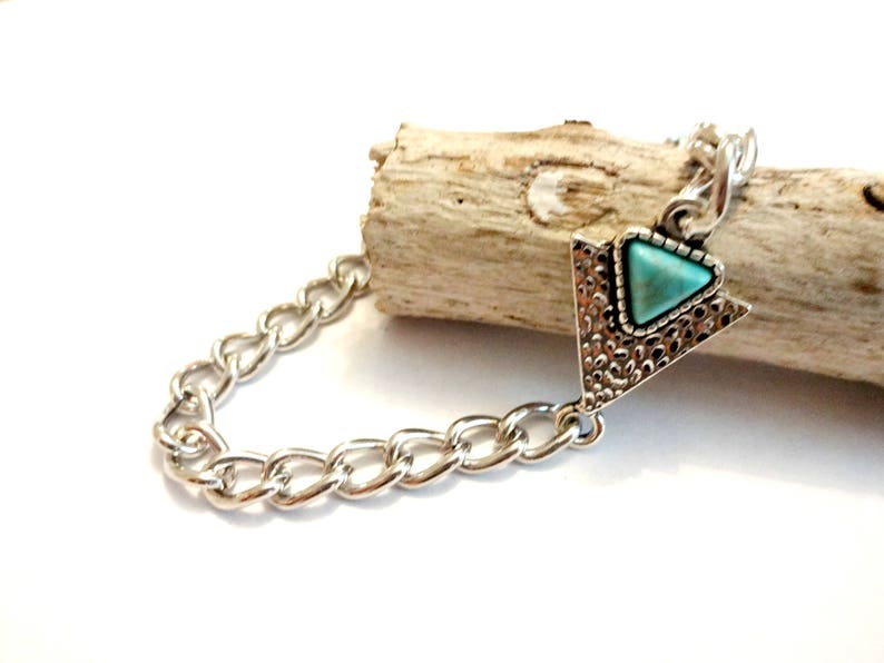 May include: A silver chain bracelet with a turquoise triangle pendant. The pendant has a textured silver design.