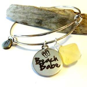 May include: Silver expandable bangle bracelet with a charm that says "Beach Babe" with flip flop icons, a small charm with the letter "R" and a yellow stone charm.