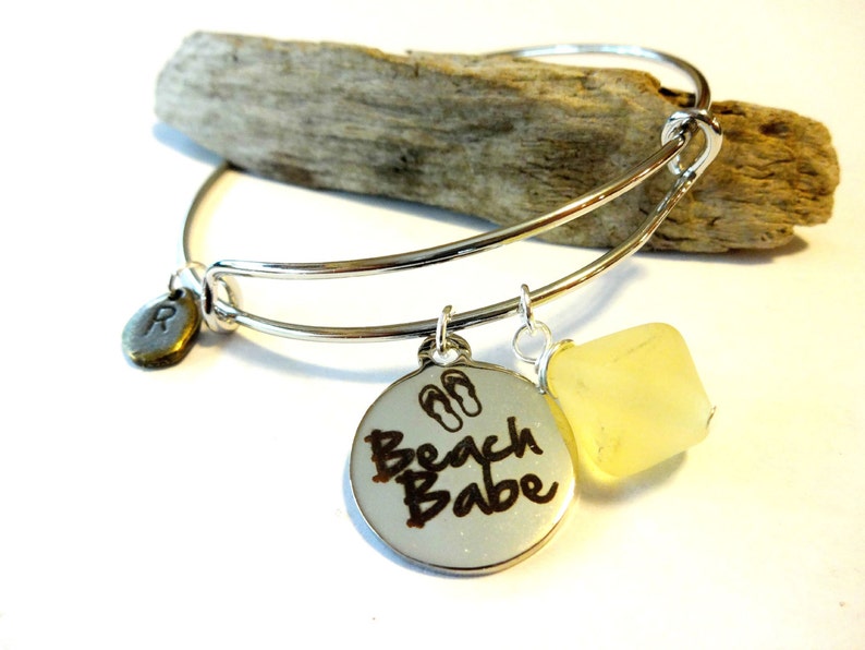 May include: Silver expandable bangle bracelet with a charm that says "Beach Babe" with flip flop icons, a small charm with the letter "R" and a yellow stone charm.
