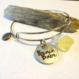 May include: Silver bangle bracelet with a charm that says "Beach Babe" with flip-flop symbols and a yellow gemstone charm.