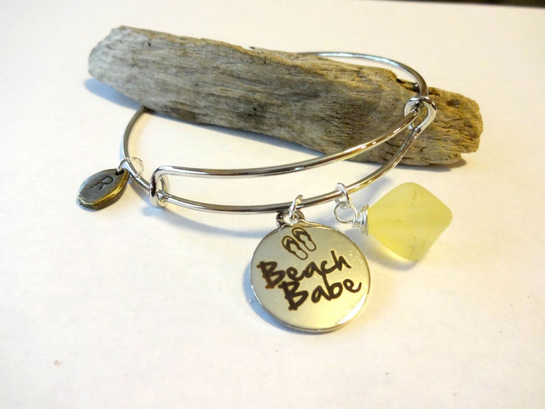 May include: Silver bangle bracelet with a charm that says "Beach Babe" with flip-flop symbols and a yellow gemstone charm.