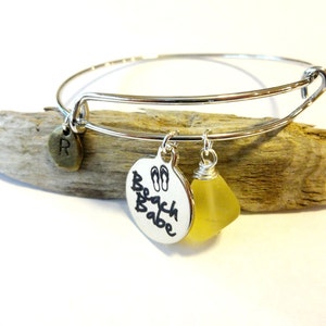 May include: Silver charm bracelet with a yellow glass bead, a charm with the text "Beach Babe" and flip-flop symbols, and a charm with the letter "R".
