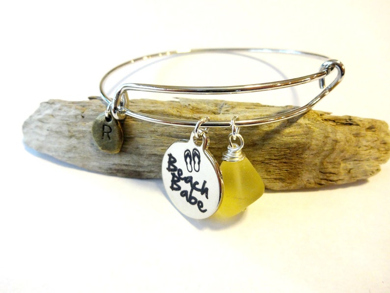 May include: Silver charm bracelet with a yellow glass bead, a charm with the text "Beach Babe" and flip-flop symbols, and a charm with the letter "R".