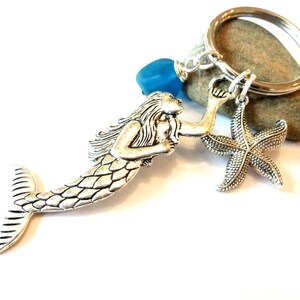 May include: Silver mermaid charm with a blue glass bead and a silver starfish charm attached to a silver key ring.