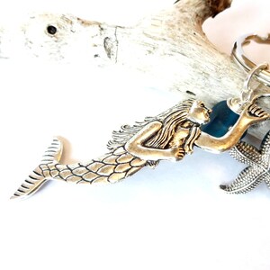 May include: Silver mermaid keychain with a starfish charm and a blue glass bead. The mermaid is holding a seashell.
