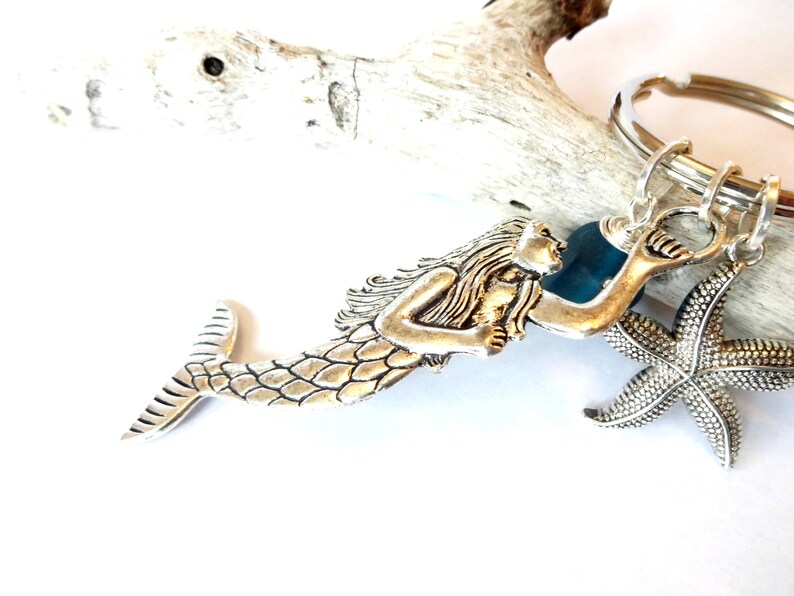 May include: Silver mermaid keychain with a starfish charm and a blue glass bead. The mermaid is holding a seashell.