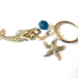 May include: Silver mermaid charm keychain with a blue glass bead, a silver starfish charm, and a silver key ring.