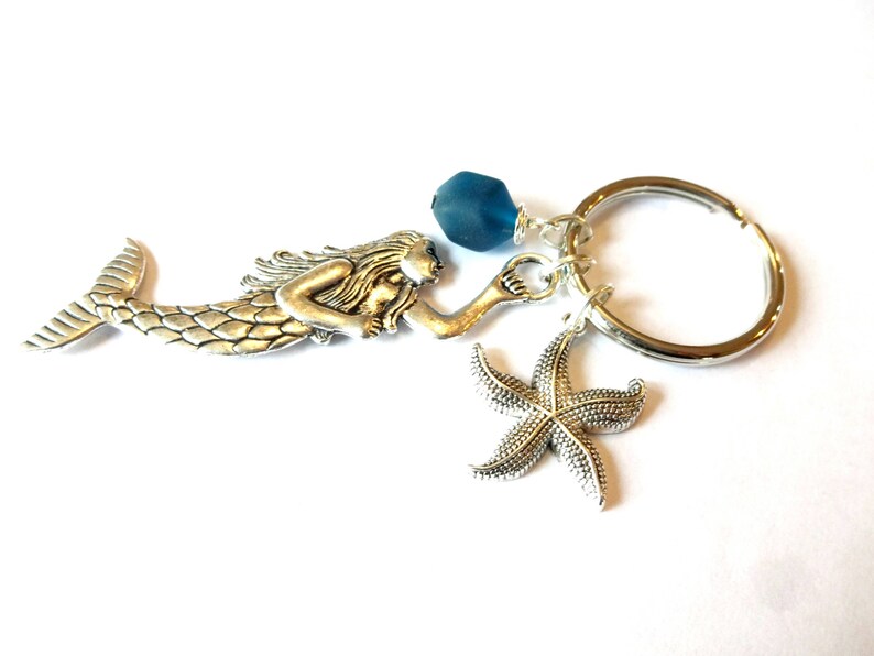 May include: Silver mermaid charm keychain with a blue glass bead, a silver starfish charm, and a silver key ring.