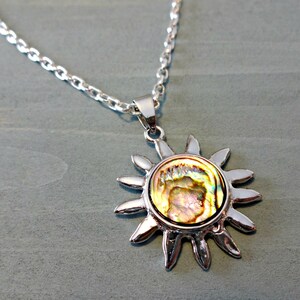 Op de afbeelding: Een zilveren ketting met een zonvormige hanger met een iriserende abalone-schelp.