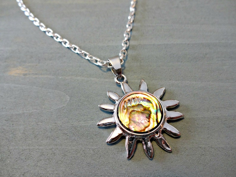 Op de afbeelding: Een zilveren ketting met een zonvormige hanger met een iriserende abalone-schelp.
