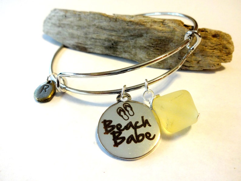 May include: Silver charm bracelet with a round charm that says "Beach Babe" with flip-flop symbols, a small round charm with the letter "R" and a yellow glass bead.
