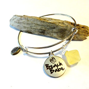 May include: Silver charm bracelet with a charm that says "Beach Babe" with flip-flop icons, a small oval charm with the letter "R" and a yellow stone charm.