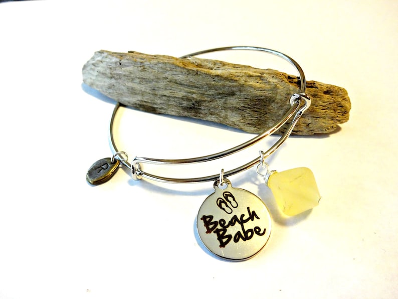 May include: Silver charm bracelet with a charm that says "Beach Babe" with flip-flop icons, a small oval charm with the letter "R" and a yellow stone charm.