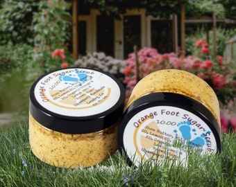 May include: Two jars of orange foot sugar scrub with a yellow and brown sugar base. The jars have black lids and white labels with the text "Orange Foot Sugar Scrub" and the price "10.00".