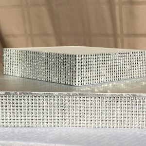 Könnte beinhalten: Zwei-stöckiger Kuchenständer mit silberner Oberfläche und einem diamantartigen Muster an den Rändern.