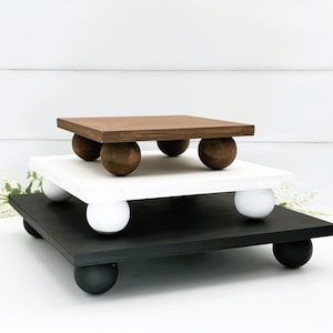 Puede incluir: Un expositor de madera de tres niveles con patas redondas. El nivel superior es marrón, el nivel intermedio es blanco y el nivel inferior es negro.