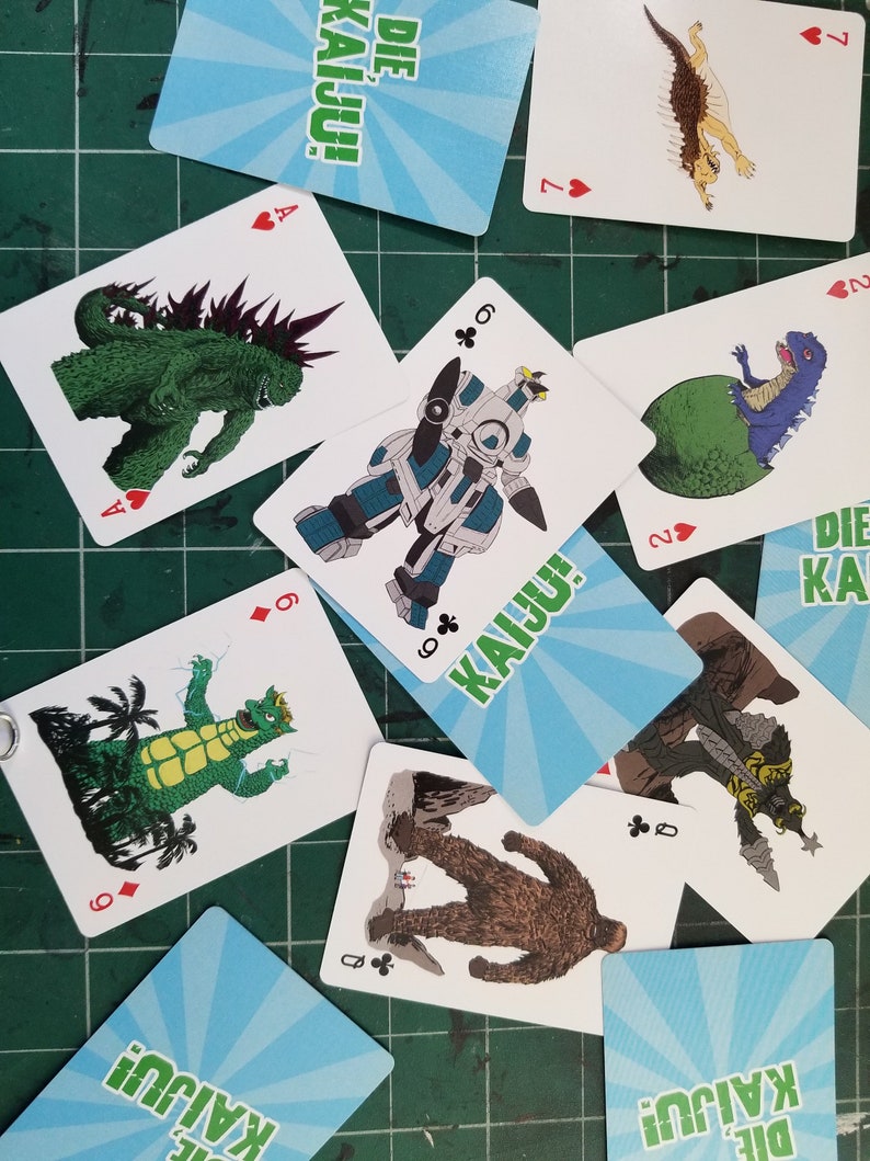 May include: A collection of playing cards featuring illustrations of various monsters and creatures. The cards have a white background with colorful images and suit symbols. Some cards display the text "DIE KAIJU!" and "KAIJU!".