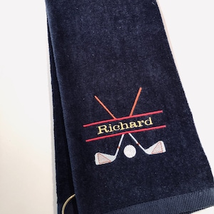 May include: Navy blue golf towel with a red and orange embroidered golf club design and the name "Richard" in yellow thread.