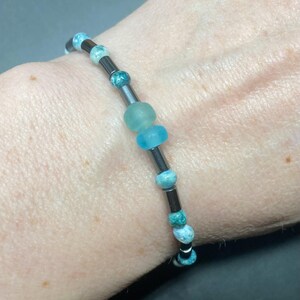 Op de afbeelding: Een armband met blauwe en zwarte kralen. De armband is gemaakt van hematiet en glazen kralen. De kralen zijn rond en hebben een gladde afwerking.
