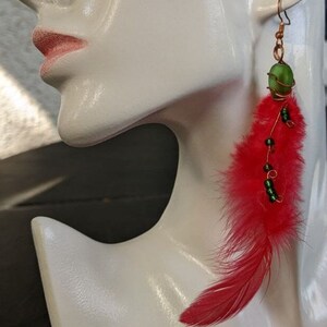 May include: Red feather earrings with a green glass bead and copper wire accents.