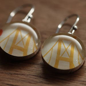 May include: A pair of silver earrings with a white background and a gold bridge design. The earrings are round and have a silver hook.