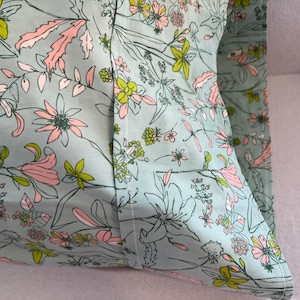 May include: A light blue pillowcase with a floral pattern featuring pink and green flowers. The pillowcase has a white seam down the centre.