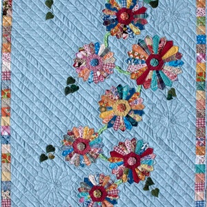 May include: A blue quilt with a design of colorful flowers made from fabric scraps. The flowers are arranged in a vine-like pattern and have a button in the center.