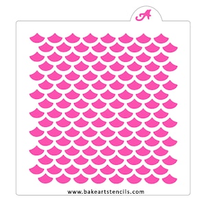 May include: A white plastic stencil with a pink mermaid scale pattern. The stencil is designed for use with frosting or paint to create a decorative design on cakes, cookies, or other baked goods. The stencil is approximately 8 inches wide and 10 inches tall. The text "www.bakeartstencils.com" is printed at the bottom of the stencil.