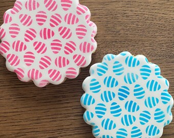 May include: Two round sugar cookies decorated with a pattern of pink and blue stripes. The cookies are on a wooden surface.