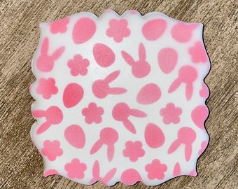 May include: A white cookie decorated with a pink Easter-themed pattern. The pattern includes bunnies, eggs, and flowers.