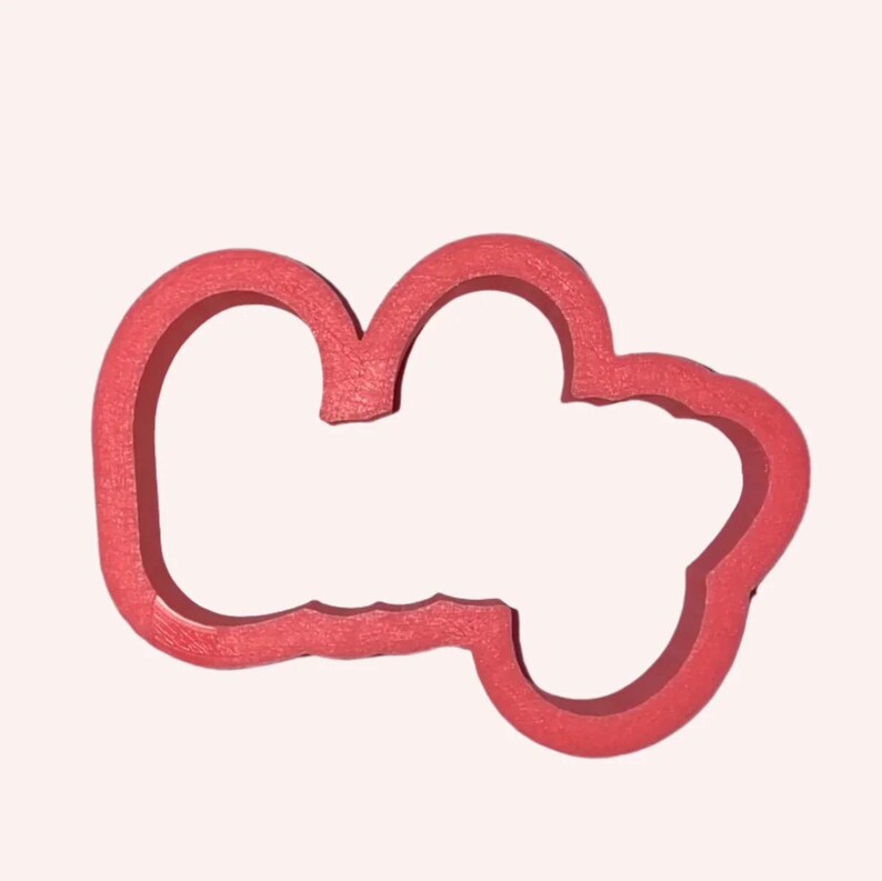 May include: A red cookie cutter with a textured surface, featuring an irregular, rounded, cloud-like shape with three distinct lobes and a hollow centre, designed for cutting dough into a specific outline for baking and food preparation.