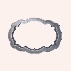 May include: A silver-colored metal cookie cutter shaped like a decorative oval frame. The cutter has a smooth, slightly textured surface.